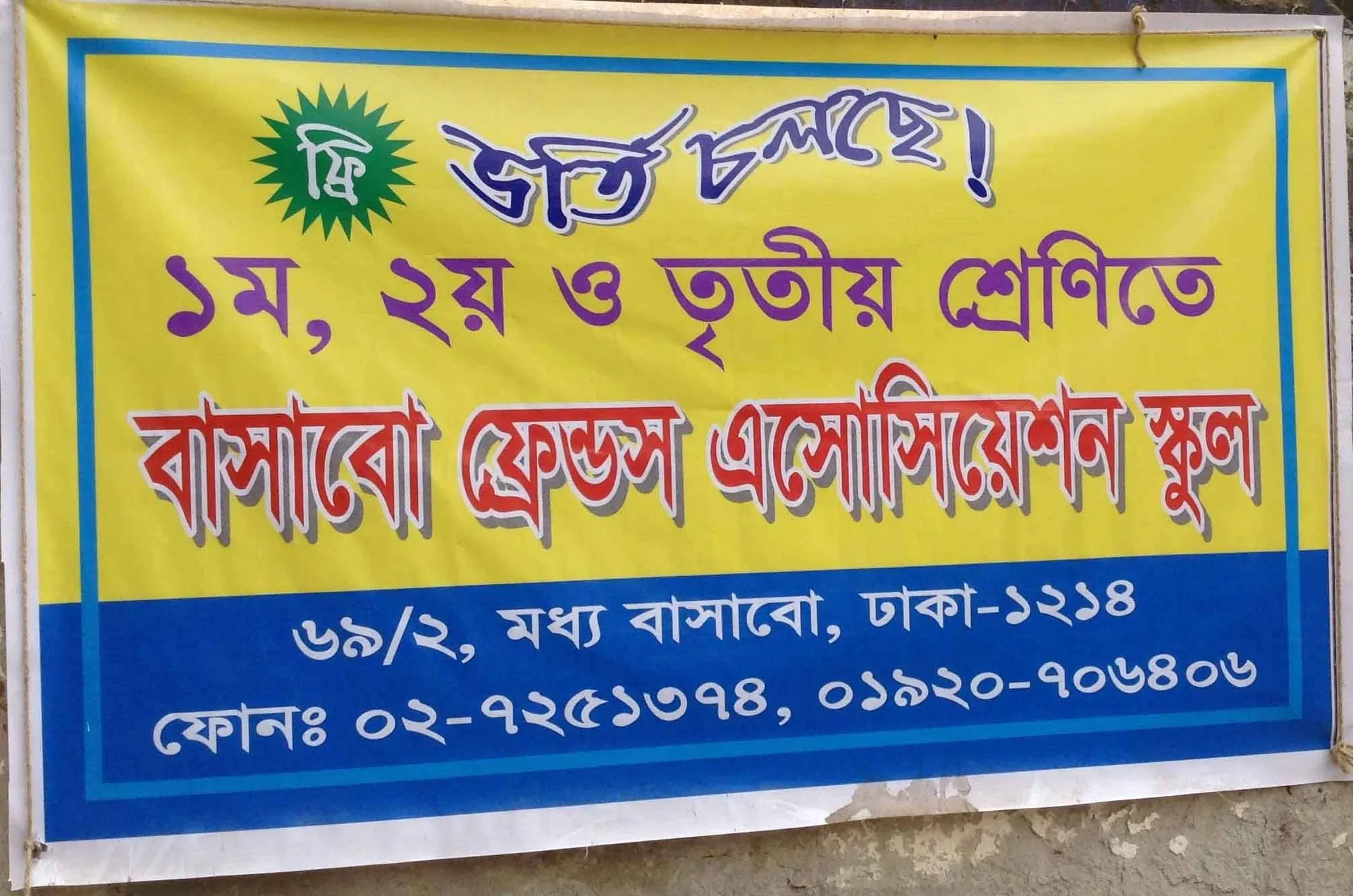 Yellow and blue banner in Bangla announcing free admission to classes 1, 2 and 3 at the Bashaboo Friends Association School, 69/2 Central Bashabo, Dhaka-1214, with the school’s phone numbers